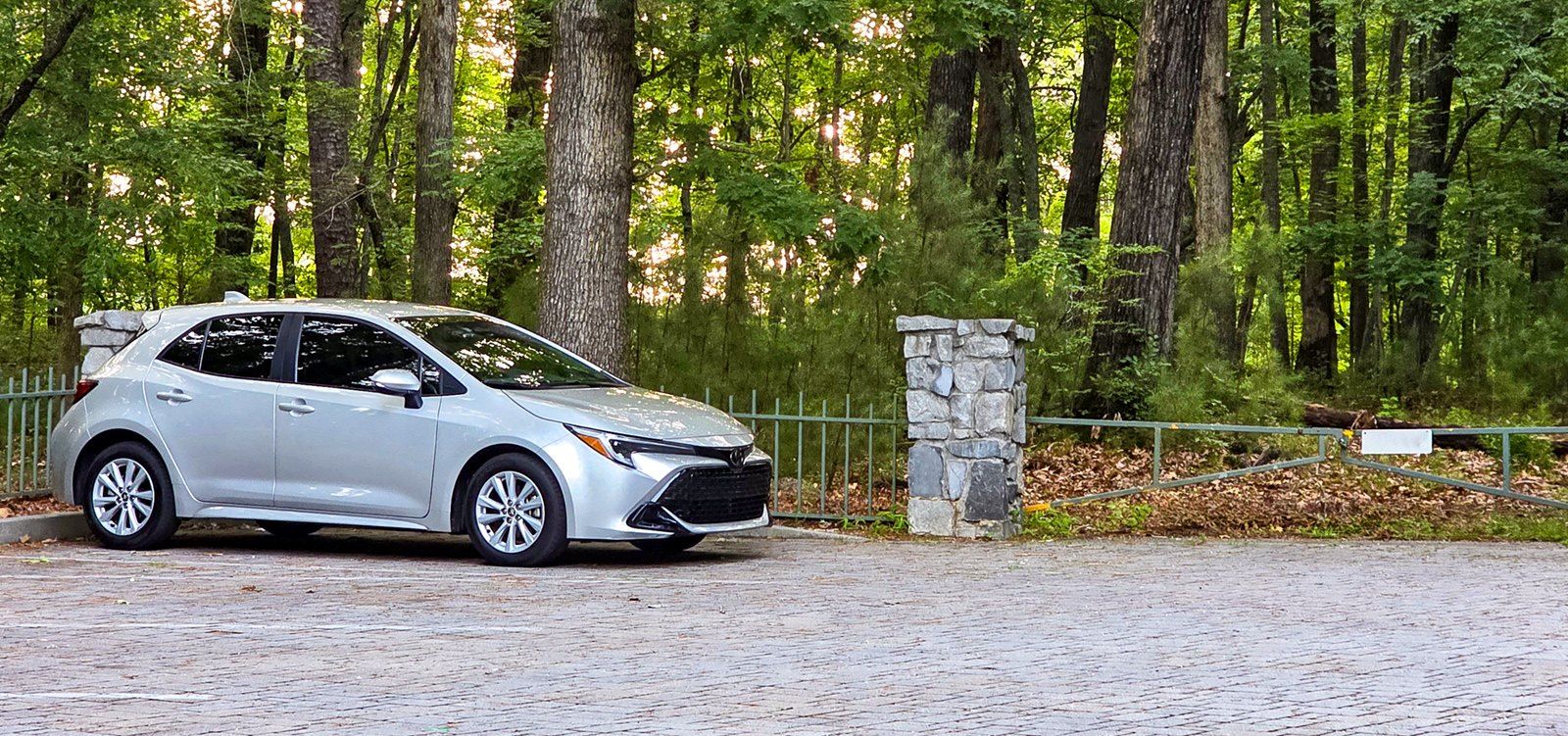 The 2023 Corolla parked by a stone gatepost at the edge of the woods